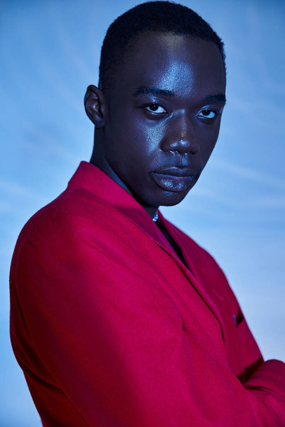 модний красивий афроамериканський чоловік в червоному яскравому блістері позує на синьому водяному фоні - Фото, зображення
