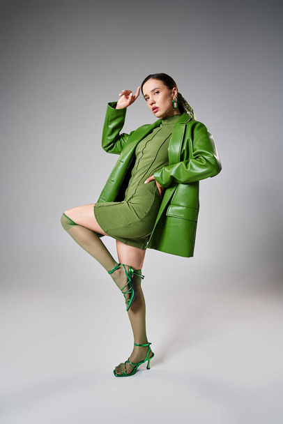 Full length φωτογραφία της γυναίκας σε πράσινο μίνι φόρεμα, δερμάτινο μπουφάν, κάλτσες γόνατο ποζάροντας λαμπρά - Φωτογραφία, εικόνα