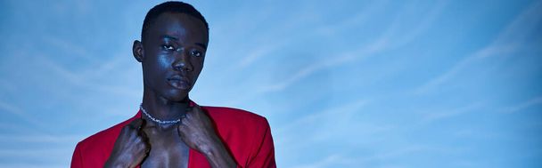 trendy african american man in red vibrant blazer posing on blue watery background, banner - Photo, Image