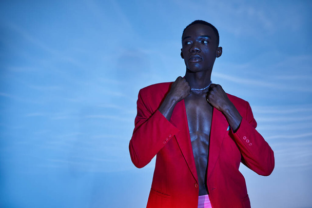 stijlvol jong Afrikaans amerikaans man in roze broek en rode blazer weg te kijken op waterige achtergrond - Foto, afbeelding