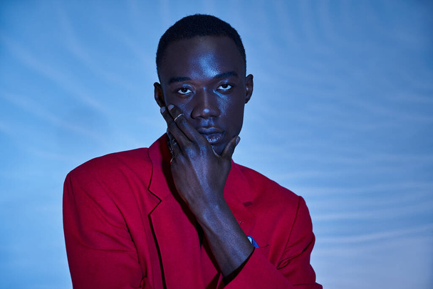 Kırmızı renkli ceketli, mavi sulu arka planda poz veren Afro-Amerikan bir adam. - Fotoğraf, Görsel
