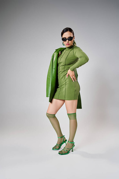 Pełna długość zdjęcie ładnej kobiety w całości zielony modny wygląd i czarne okulary przeciwsłoneczne na szarym tle - Zdjęcie, obraz