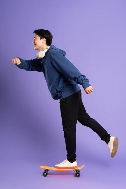 Imagen del joven asiático jugando al skate sobre fondo púrpura - Foto, Imagen