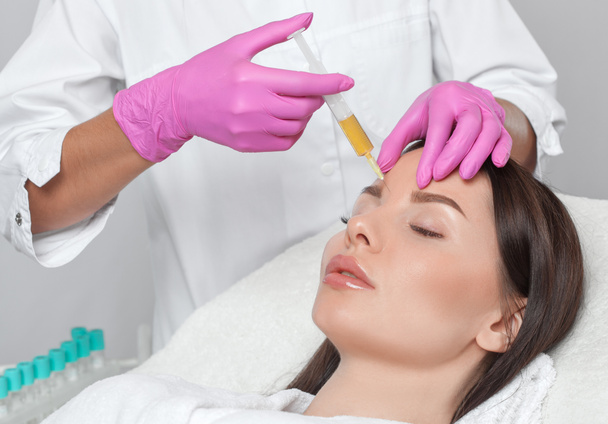 Cosmetoloog doet prp therapie op het gezicht van een mooie vrouw in een schoonheidssalon. Cosmetologisch concept. - Foto, afbeelding