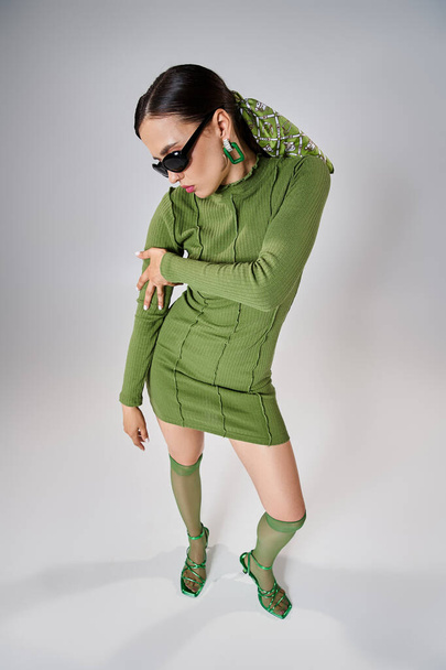 Top kilátás hölgy zöld mini ruha és térd zokni, visel fekete szemüveg szürke háttér - Fotó, kép