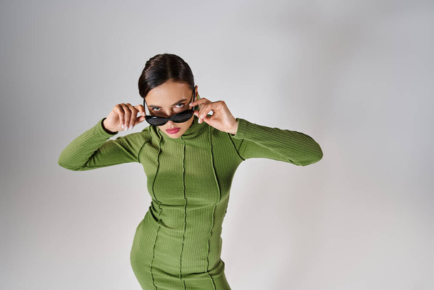 Top view of woman in green outfit, touching her eyewear with both hands and looking at camera - Photo, Image