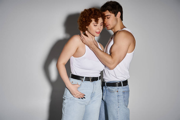 Houkutteleva seksikäs pari sinisissä farkuissa poseeraa yhdessä rakastavasti harmaalla taustalla, suhde - Valokuva, kuva