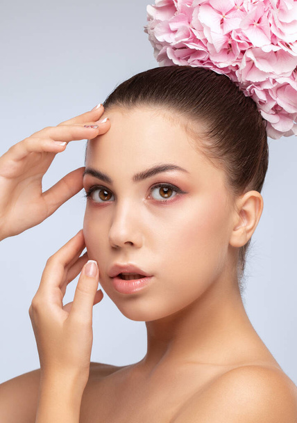 Portret van een mooie brunette met een gezonde schone huid en frisse make-up. Ze houdt een roze hortensia bij haar gezicht. Esthetische kosmetologie en make-up concept. - Foto, afbeelding
