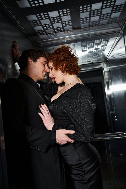 エレベーターで抱擁エレガントな黒の服装で楽しいボーイフレンドとガールフレンドを魅了, セクシーなカップル - 写真・画像