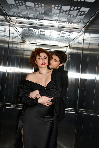 заманчивые любящий парень и девушка в элегантных черных одеждах обнимаясь в лифте, сексуальная пара - Фото, изображение