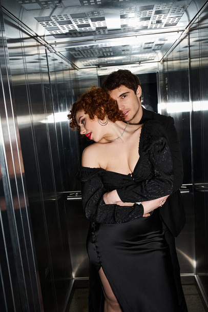 エレベーターで抱擁エレガントな黒の服装で愛するボーイフレンドとガールフレンドを魅了, セクシーなカップル - 写真・画像