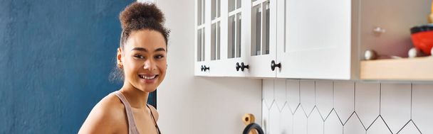 vreugdevol mooi Afrikaans amerikaans vrouw in homewear glimlachen gelukkig op camera in de keuken, banner - Foto, afbeelding