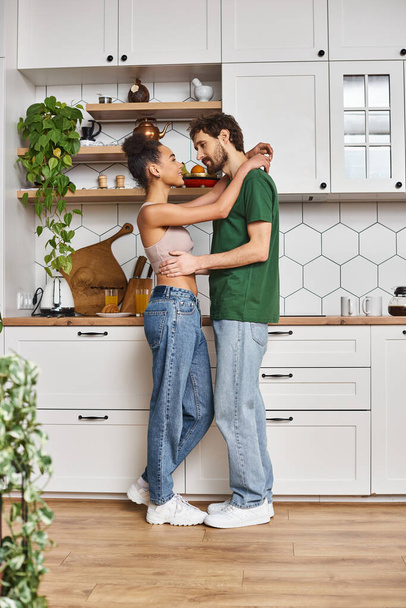 freudig attraktives interrassisches Paar in lässiger Kleidung, das sich vor dem Frühstück liebevoll umarmt - Foto, Bild