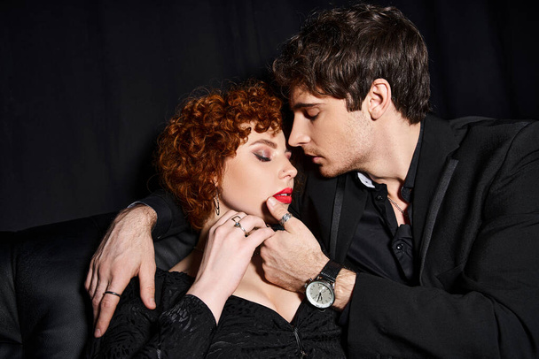 angażujący chłopak i dziewczyna w eleganckie ubrania przytulając się z miłością na czarnej kanapie, sexy para - Zdjęcie, obraz