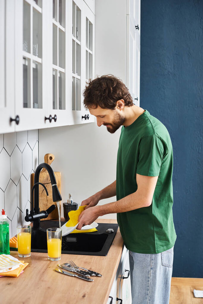 hombre guapo alegre en platos de lavado de ropa cómoda después del desayuno en casa en la cocina - Foto, imagen