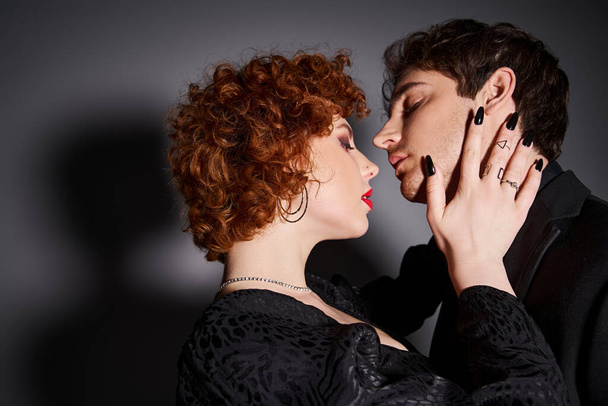 привлекательная сексуальная пара в черных элегантных одеждах, готовящаяся поцеловать друг друга на сером фоне - Фото, изображение