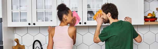alegre atraente multirracial namorada e namorado no confortável homewear fazendo tarefas na cozinha - Foto, Imagem