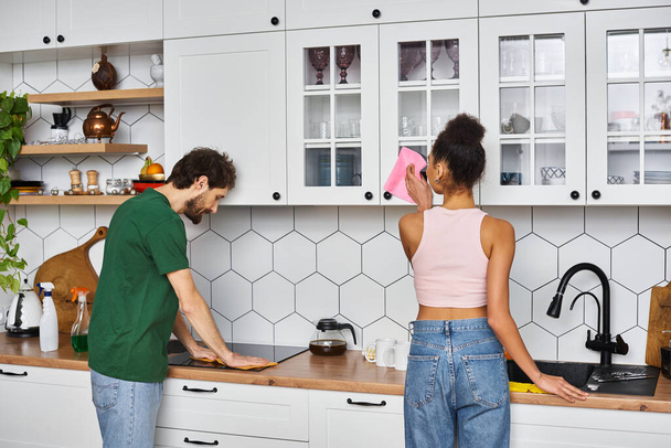 good looking diverse jolly couple in homewear during spring cleaning at home smiling happily - Photo, Image
