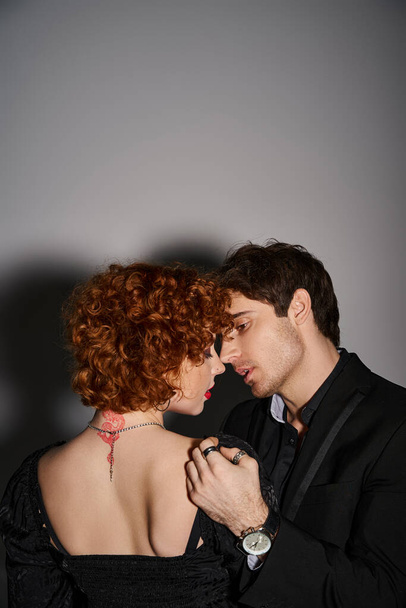 atractivo sexy pareja en negro elegante trajes besándose y abrazándose amorosamente en gris fondo - Foto, Imagen