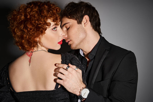 соблазнительная сексуальная пара в черных элегантных одеждах целуется и обнимается с любовью на сером фоне - Фото, изображение
