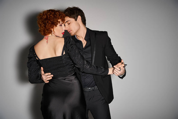 schönes sexy Paar in schwarzen eleganten Kleidern küsst und umarmt sich liebevoll auf grauem Hintergrund - Foto, Bild