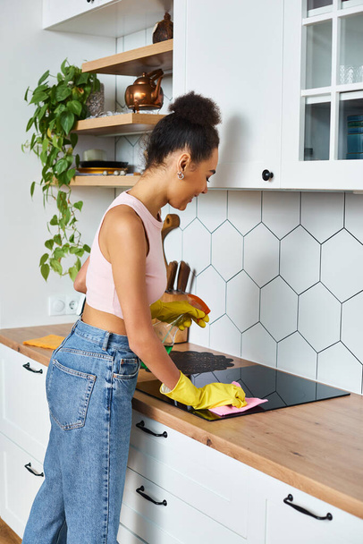 красива весела афроамериканка в затишному домашньому одязі миє плиту під час весняного прибирання - Фото, зображення