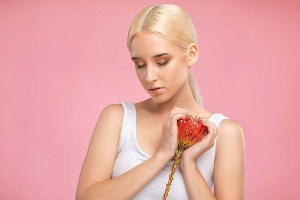 Portrait of a beautiful blonde girl with healthy clean skin and fresh make-up. She holds a flower in her hand. Aesthetic cosmetology and makeup concept. - Photo, Image