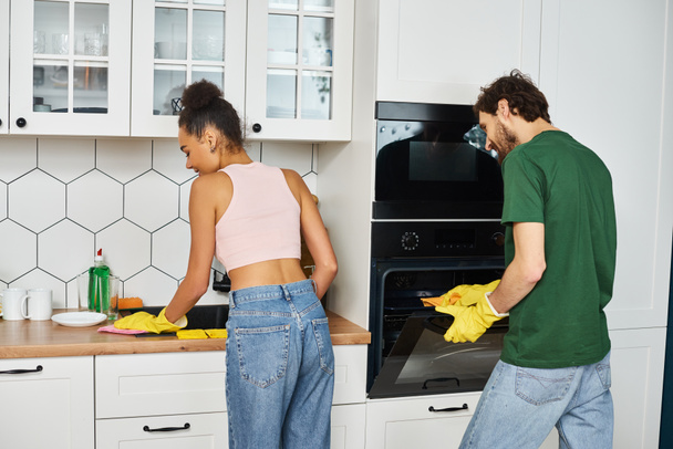 Весьма красивая межрасовая пара в домашней одежде тщательно убирает посуду дома - Фото, изображение