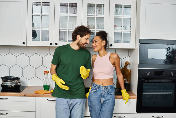 appealing multicultural jolly couple in casual attires smiling at each other during spring cleaning - Photo, Image