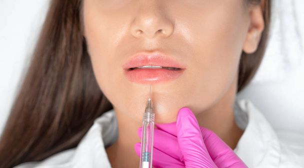 Cosmetologist does injections for lips augmentation and anti wrinkle in the nasolabial folds of a beautiful woman. Women's cosmetology in the beauty salon. - Photo, Image