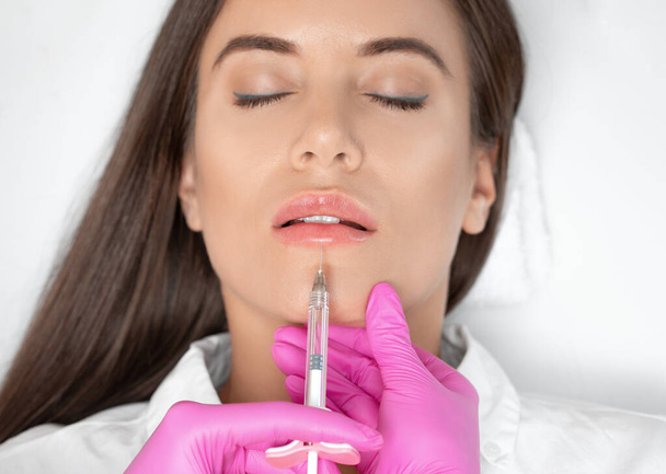 Cosmetoloog doet injecties voor lippen vergroting en anti rimpel in de nasolabiale plooien van een mooie vrouw. Cosmetologie van vrouwen in de schoonheidssalon. - Foto, afbeelding
