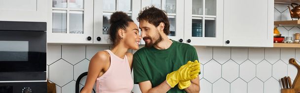 красивая межрасовая радостная пара наслаждаясь друг другом во время уборки на кухне, баннер - Фото, изображение
