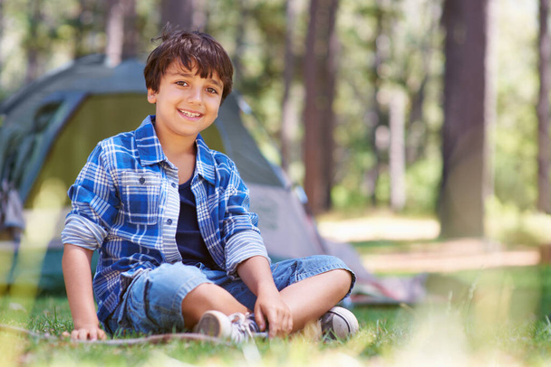 Forest camping or portrait of happy child in nature for playing, adventure or holiday vacation in park. Relax, confidence or male kid with smile in woods, garden or grass for fun hiking or wellness. - Photo, Image