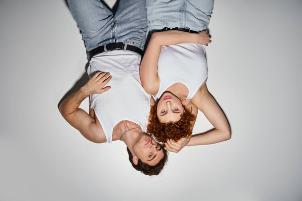 verleidelijke man en vrouw in blauwe jeans liggend samen op de vloer en kijkend naar camera, sexy koppel - Foto, afbeelding