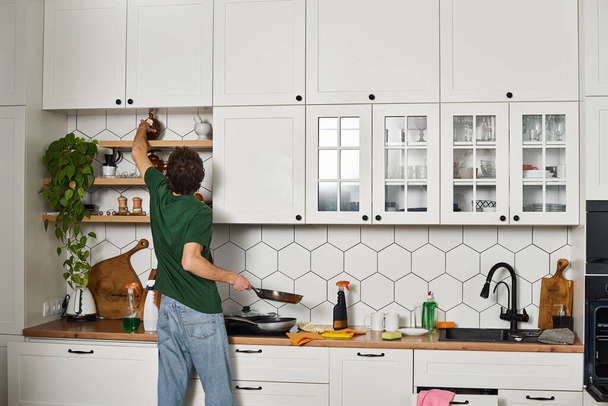 πίσω όψη του ανθρώπου σε casual σκούρο πράσινο t πουκάμισο κάνει δουλειές στην κουζίνα κατά τη διάρκεια της άνοιξης καθαρισμού - Φωτογραφία, εικόνα