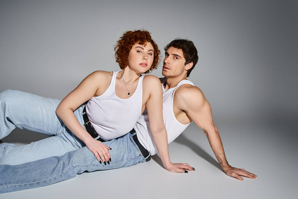 привлекательная сексуальная пара в удобных синих джинсах, лежащих на полу вместе и смотрящих в камеру - Фото, изображение