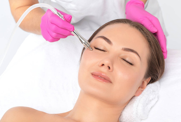 Cosmetoloog maakt procedure microdermabrasie op het gezicht tegen acne en mee-eters in de buurt van de ogen. Cosmetologie van vrouwen in de schoonheidssalon. - Foto, afbeelding