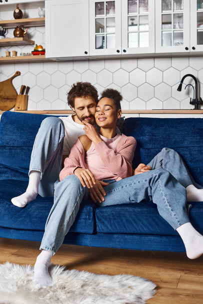 自宅でソファーで暖かく抱擁する快適なホームウェアで良い見た目に満足したカップル - 写真・画像
