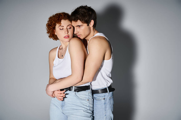 привлекательный парень и девушка в повседневной одежде обнимаются с любовью на сером фоне, сексуальная пара - Фото, изображение