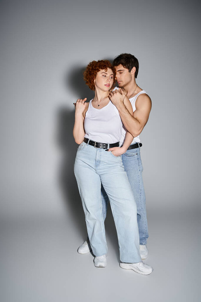 Charmanter Freund und Freundin in lässiger Kleidung, die sich vor grauem Hintergrund liebevoll umarmen, sexy Paar - Foto, Bild