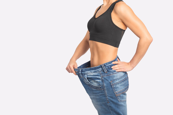 Zayıflayan genç kadın kilo verdikten sonra yaşlı pantolonun boyutunu gösteriyor. Düzgün beslenme ve sağlıklı yaşam tarzı kavramı. - Fotoğraf, Görsel