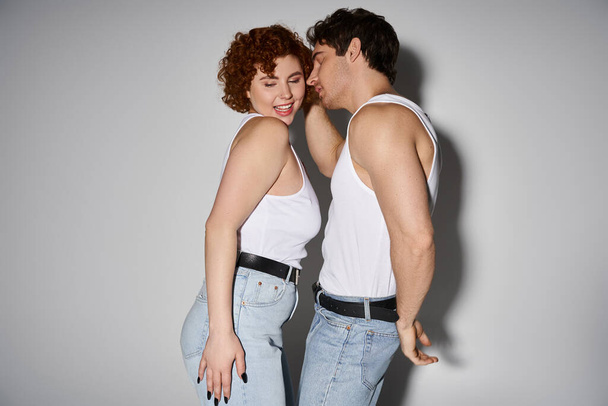alegre seductor hombre y mujer en jeans posando sobre gris telón de fondo y sonriendo felizmente, sexy pareja - Foto, imagen