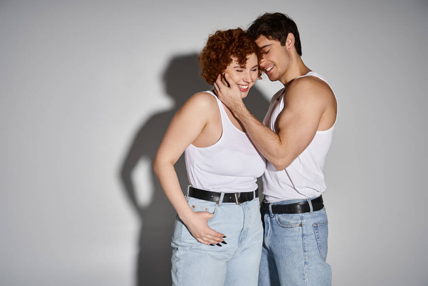 alegre seductor hombre y mujer en jeans posando sobre gris telón de fondo y sonriendo felizmente, sexy pareja - Foto, imagen