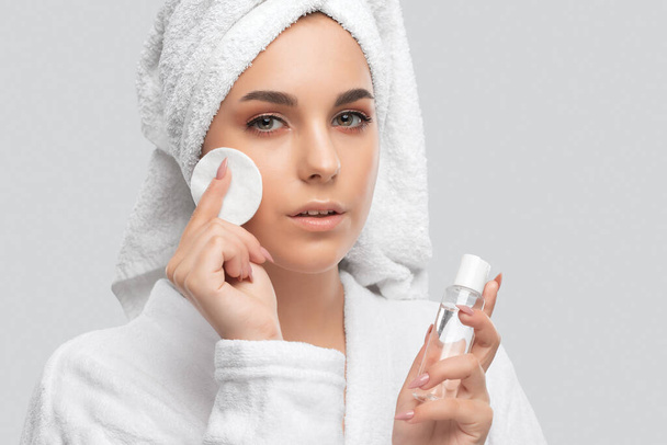 Beautiful smiling woman with clean skin holds a cotton pad. She cleanses the skin with a tonic. Cosmetology and professional skin care. - Foto, Bild