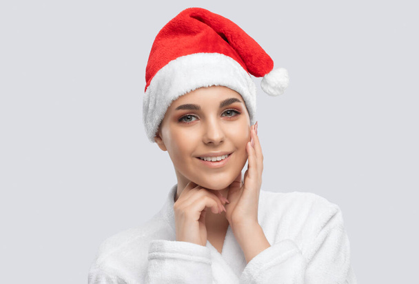 Portrait d'une belle fille brune au chapeau de Père Noël avec une peau propre et saine et un maquillage frais. Cosmétologie esthétique et concept de maquillage. - Photo, image