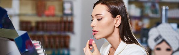 beautiful jolly woman in business casual choosing new lipstick while in cosmetics store, banner - Photo, Image