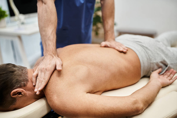 vista ritagliata del medico laborioso in vestaglia blu massaggiare il suo paziente maturo durante la riabilitazione - Foto, immagini
