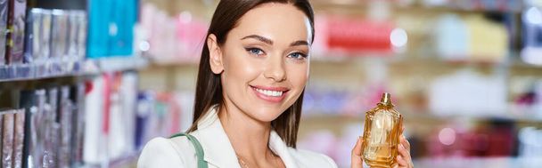 веселая привлекательная женщина выбирает парфюмерию в магазине косметики и улыбается в камеру, баннер - Фото, изображение