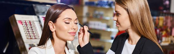 assistente de loja sedutor em blazer preto aplicando eyeliner em seu cliente enquanto na loja, banner - Foto, Imagem