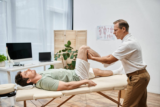 beau médecin mature vérifiant les genoux de son patient à l'hôpital, concept de réadaptation - Photo, image